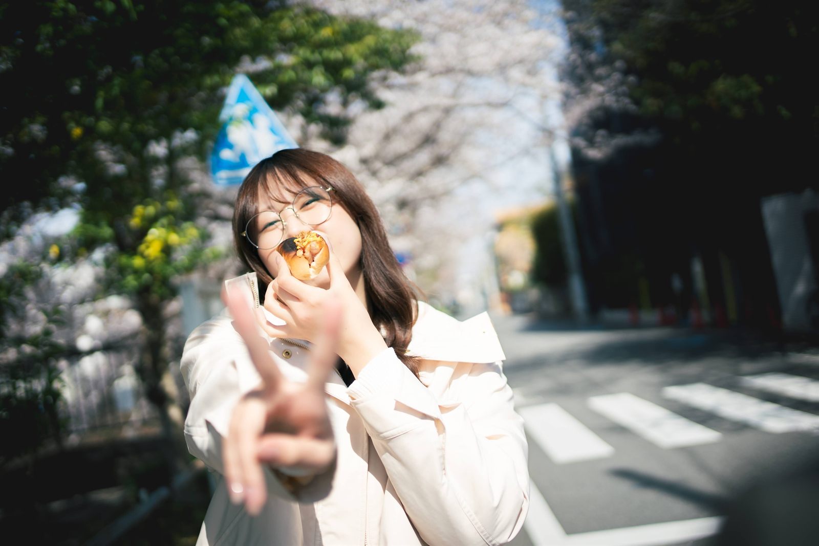 桜並木の下でパンをほおばる女性
