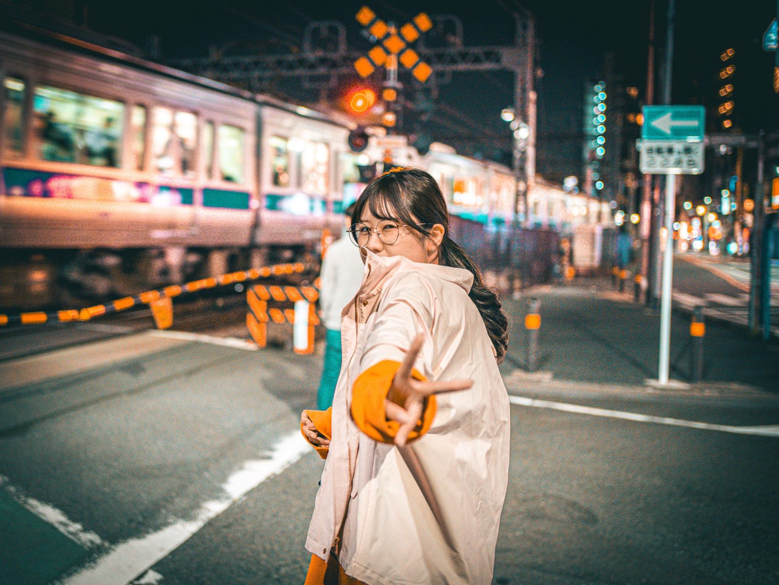 夜の踏切の前でピースサインをする女性